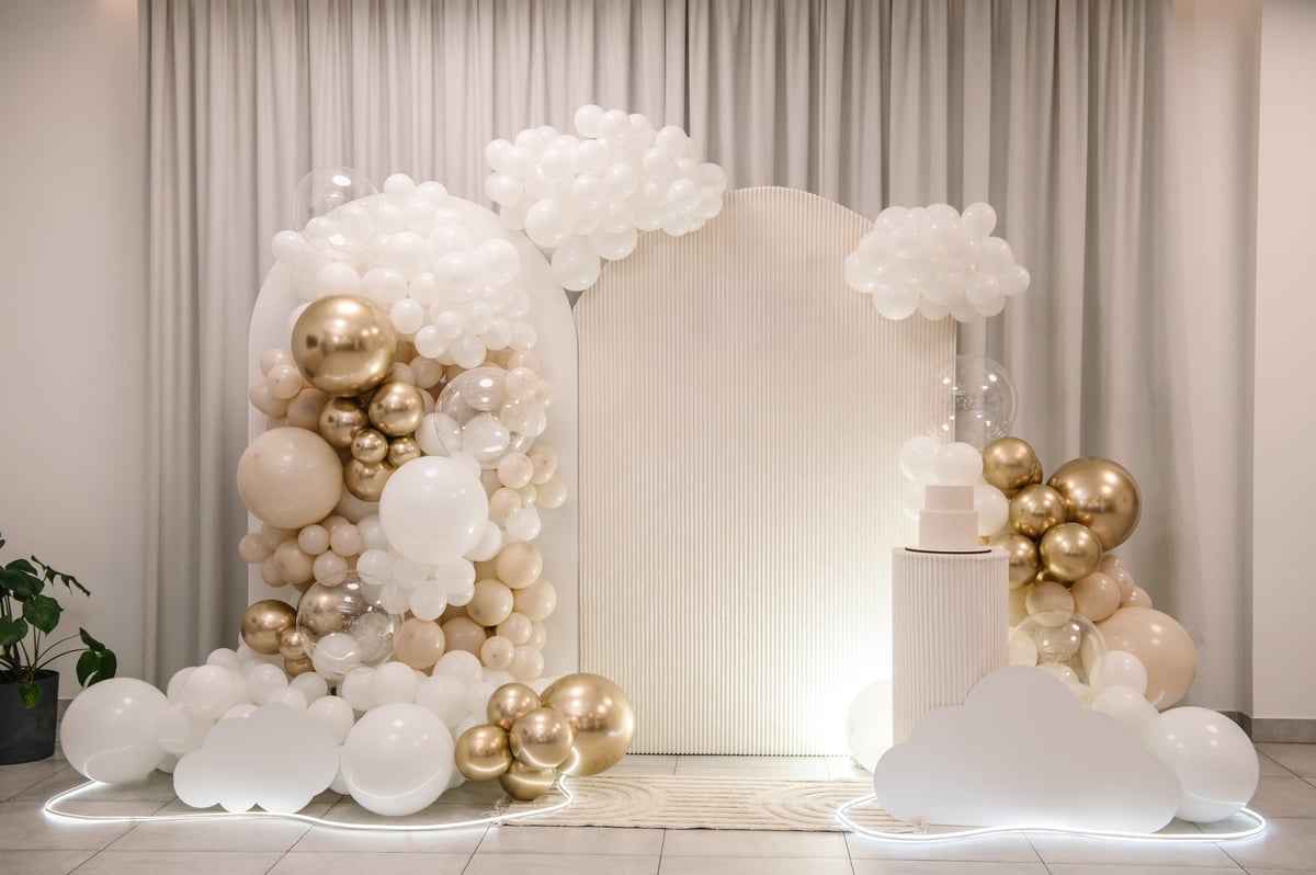 Luxurious organic balloon arch in white, beige and gold styled around a fluted backdrop and tiered cake