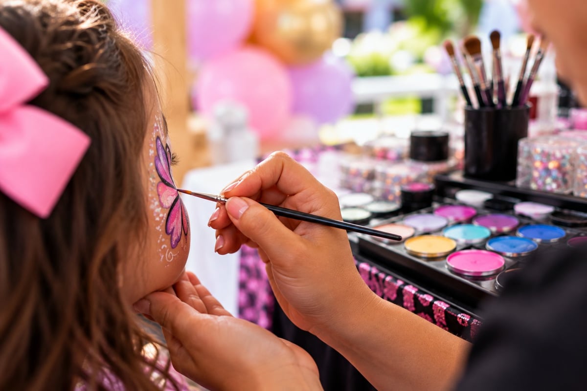 Makeup artist applying eyeshadow to a child's face at a beauty station with colorful cosmetics and decorations visible in the background