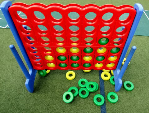 Red and blue Connect Four game board with colored checkers on green artificial turf surface
